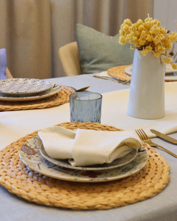 Vajilla con diseño en azul sobre mantel de lino, acompañada de servilleta beige y vela decorativa en ambiente cálido.